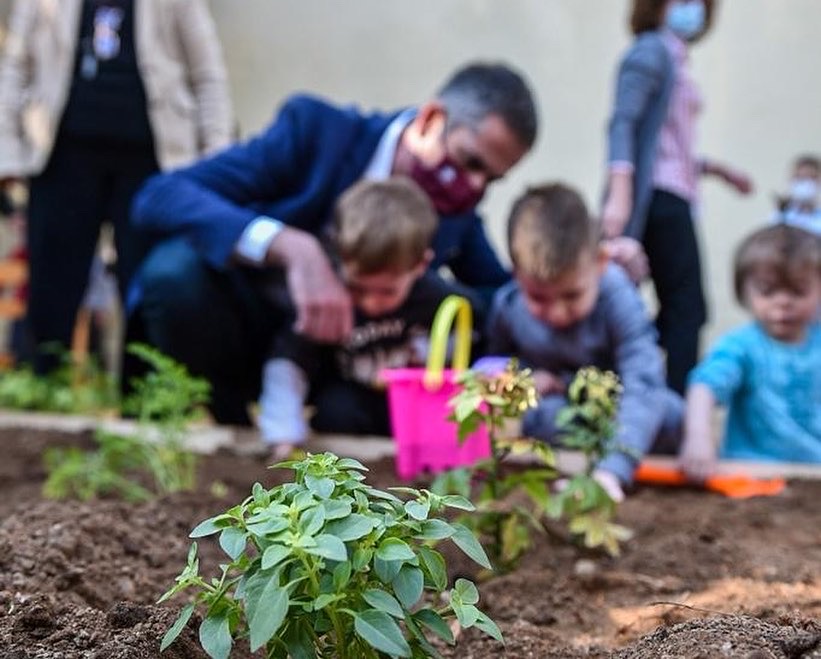 Mayor crouching with two children near the ground at the greenhouse